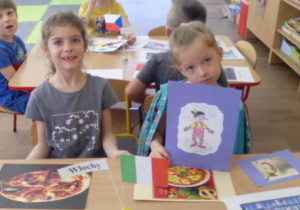 Dzieci siedzące przy stoliku z flagą Włoch i obrazkami związanymi z Włochami.